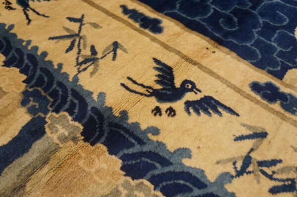 Close-up of a gold rug featuring a navy blue bird and stylized waves in medium pile.