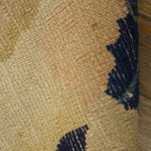 Textured rug featuring beige, faint pink, and navy blue geometric patterns folded over wood planks.