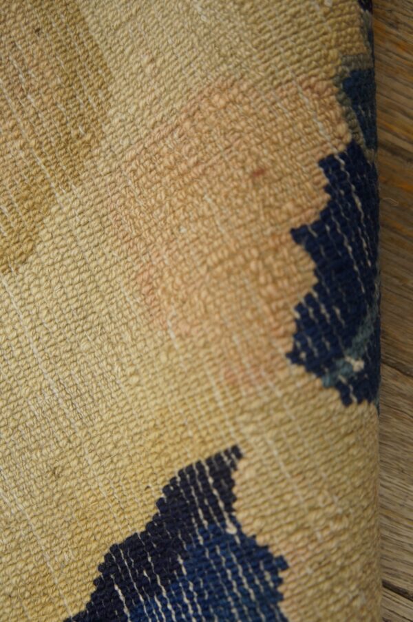 Textured rug featuring beige, faint pink, and navy blue geometric patterns folded over wood planks.