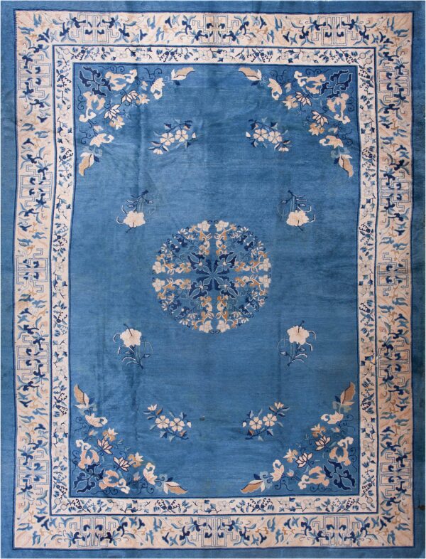 A teal blue rug featuring scattered floral designs and a wide cream border with complex geometric and vine patterns.