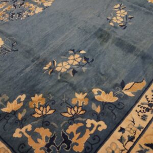Dusty blue rug with floral motifs in beige and navy, showing a detailed border and varied pile texture.