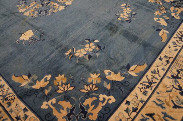 Dusty blue rug with floral motifs in beige and navy, showing a detailed border and varied pile texture.