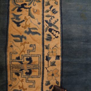 Blue rug with tan borders featuring floral and geometric patterns rests on distressed wooden planks.