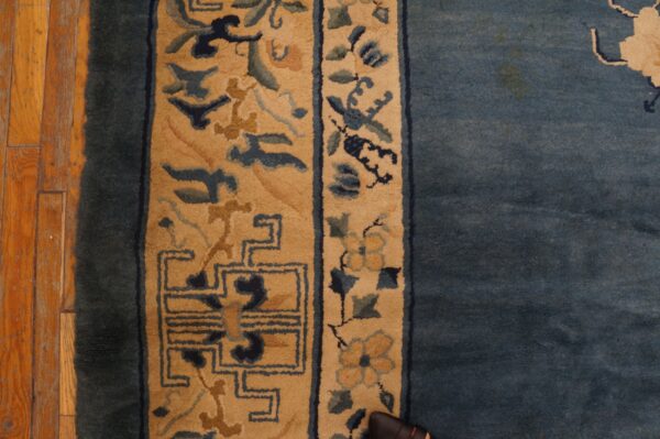 Blue rug with tan borders featuring floral and geometric patterns rests on distressed wooden planks.