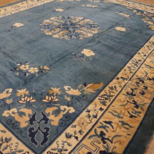 Blue rug with beige floral sprays and geometric borders rests on worn plank wood flooring.