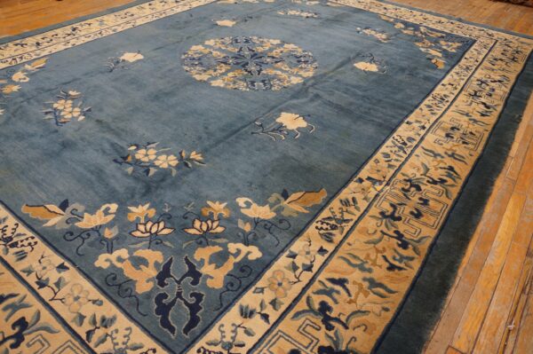 Blue rug with beige floral sprays and geometric borders rests on worn plank wood flooring.