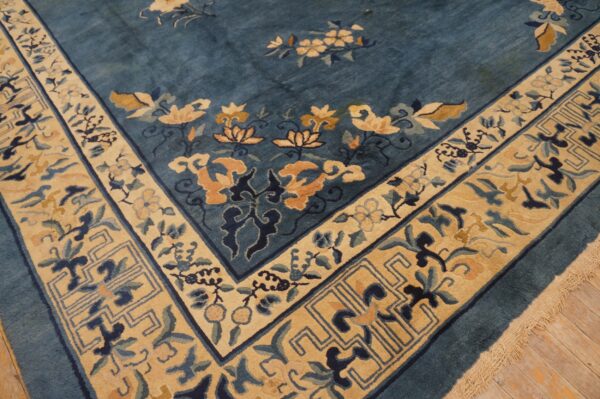 Teal rug with thick floral border featuring gold, tan, and dark blue patterns over wood flooring.