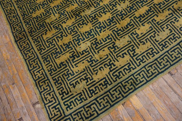 Mustard gold rug with an angular dark teal pattern and border lies on distressed wooden planks.