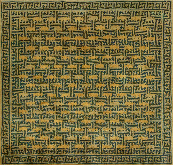 Distressed square rug in gold and dark teal, featuring a dense interlocking geometric fret pattern with borders.