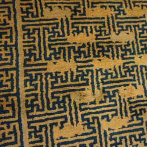 Gold and dark blue high-pile rug featuring a dense geometric fretwork pattern on wood planks.