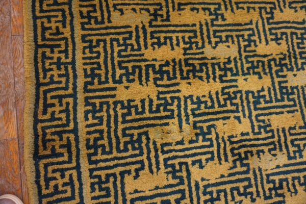 Gold and dark blue high-pile rug featuring a dense geometric fretwork pattern on wood planks.