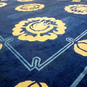 Angled view of a navy blue rug featuring large yellow stylized floral medallions and light blue stems.