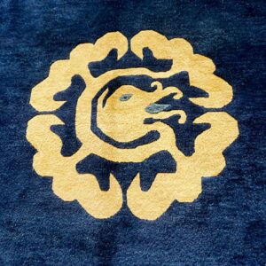 Plush dark blue rug with a centered gold dragon-like motif and subtle teal accents.