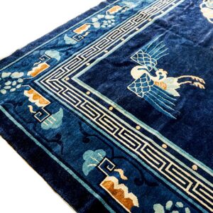 Deep blue pile rug corner with a white geometric border and stylized light blue and white crane motif.