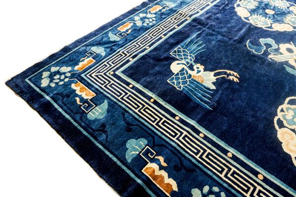 Deep blue pile rug corner with a white geometric border and stylized light blue and white crane motif.