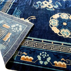 High-pile dark blue rug with light blue and tan floral patterns, folded back to reveal the weave.