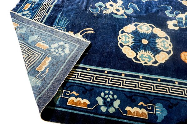 High-pile dark blue rug with light blue and tan floral patterns, folded back to reveal the weave.