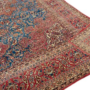 A close-up of a traditional rug featuring a deep blue field and red border with ornate floral patterns.