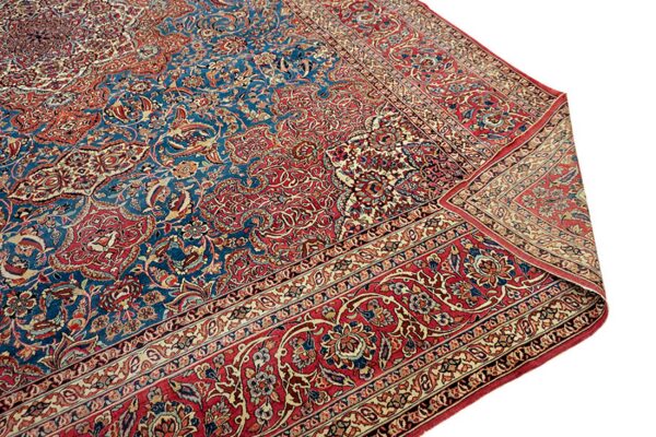 A close-up of a traditional rug featuring a deep blue field and red border with ornate floral patterns.