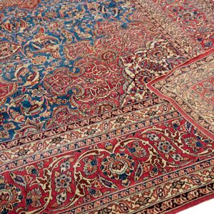 A detailed low-pile rug with blue and red floral patterns, folded to show the multiple borders.