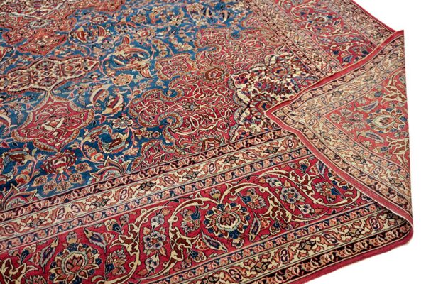 A detailed low-pile rug with blue and red floral patterns, folded to show the multiple borders.