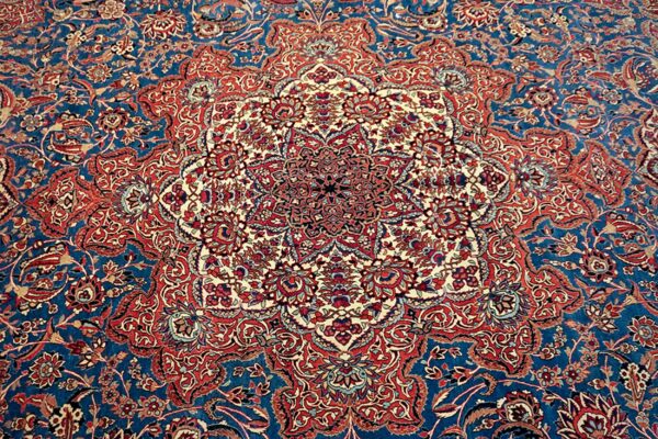 Detailed rug pattern with a large central medallion and dense red and cream florals on a deep blue field.