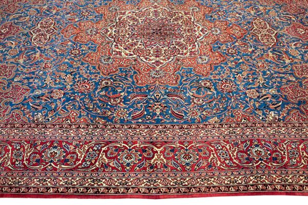 Ornate traditional rug with a deep blue field, large red border, and dense floral patterns in orange and cream.