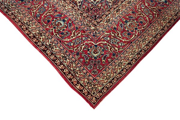 Close-up corner of a deep red rug with intricate cream and blue floral medallion and layered borders.