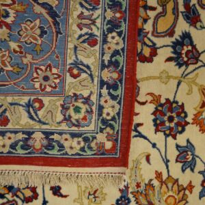 Detailed view of a rug corner, featuring a blue border panel, red trim, and an ivory floral field.