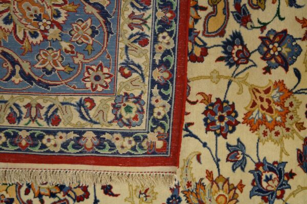 Detailed view of a rug corner, featuring a blue border panel, red trim, and an ivory floral field.