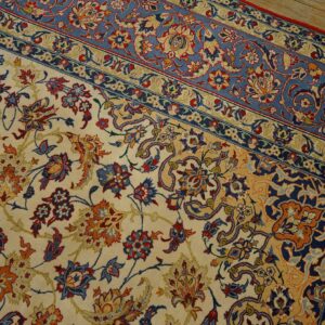Ornate cream and blue floral rug with red and gold accents resting on light wood flooring.
