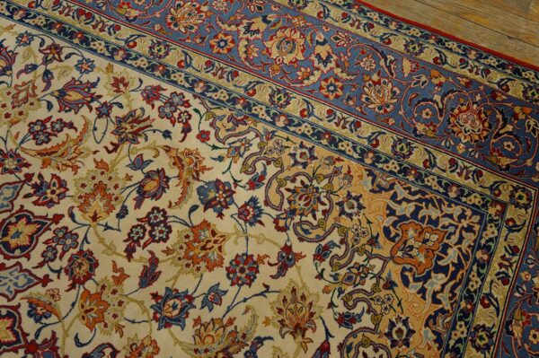 Ornate cream and blue floral rug with red and gold accents resting on light wood flooring.