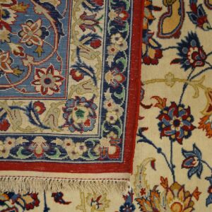 Detailed view of a blue and red low-pile border next to a cream high-pile rug with intricate floral designs.