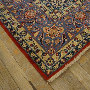 Blue rug with detailed red and cream floral patterns lies on textured light brown wood flooring.