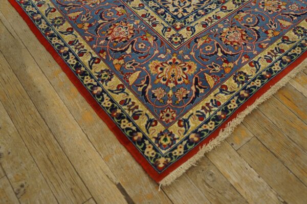 Blue rug with detailed red and cream floral patterns lies on textured light brown wood flooring.