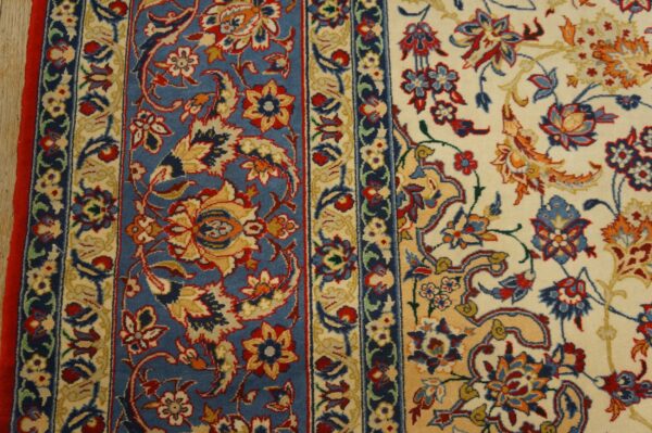 Close-up of an ornate rug featuring blue and cream fields, red borders, and detailed gold and red floral motifs.