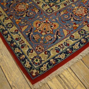 A low-pile, blue rug with detailed red and gold floral motifs lies on light, distressed wood planks.