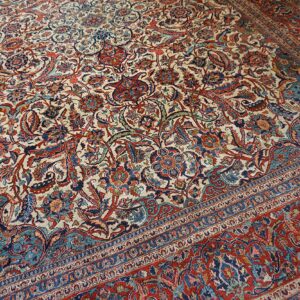 Intricately patterned rug featuring an ivory field filled with detailed red, blue, and teal floral designs.