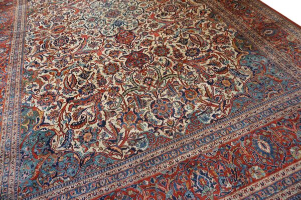 Intricately patterned rug featuring an ivory field filled with detailed red, blue, and teal floral designs.