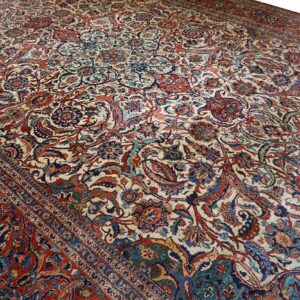 Cream rug with an all-over traditional design of scrolling vines, deep red, and blue motifs.