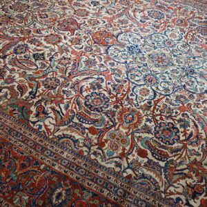 Intricate floral and paisley patterned rug with a cream ground and a wide red multi-banded border.