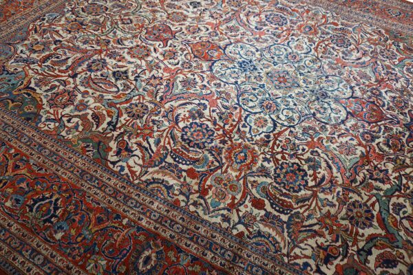 Intricate floral and paisley patterned rug with a cream ground and a wide red multi-banded border.
