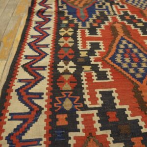 Geometric flatweave rug featuring red, navy, and cream patterns resting on worn light wood flooring.