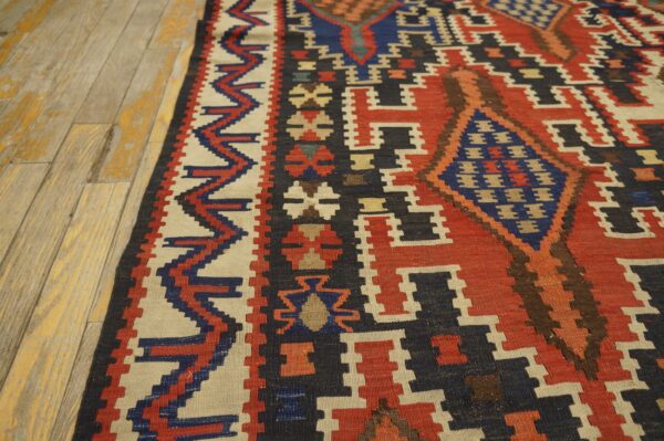 Geometric flatweave rug featuring red, navy, and cream patterns resting on worn light wood flooring.