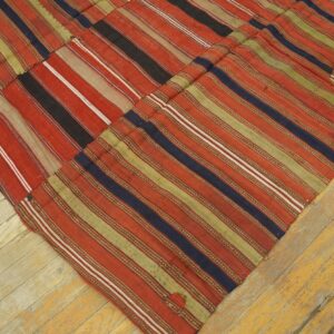 Flatweave rug with stitched panels of red, green, and blue stripes rests on yellow wood planks.