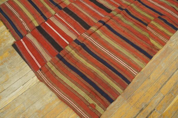 Flatweave rug with stitched panels of red, green, and blue stripes rests on yellow wood planks.