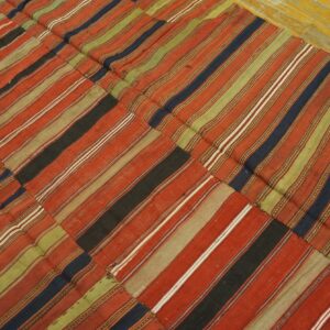 Patchwork low-pile rug featuring wide stripes in red, olive green, navy, and black on yellow wood flooring.