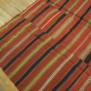 Patchwork flatweave rug featuring vertical stripes of red, olive, navy, and black colors on wooden flooring.