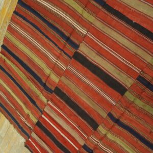 Patchwork flatweave rug with thick stripes of red, olive green, and navy on distressed plank flooring.