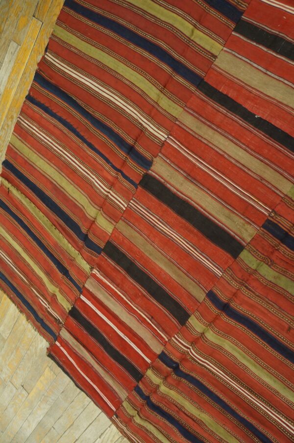 Patchwork flatweave rug with thick stripes of red, olive green, and navy on distressed plank flooring.